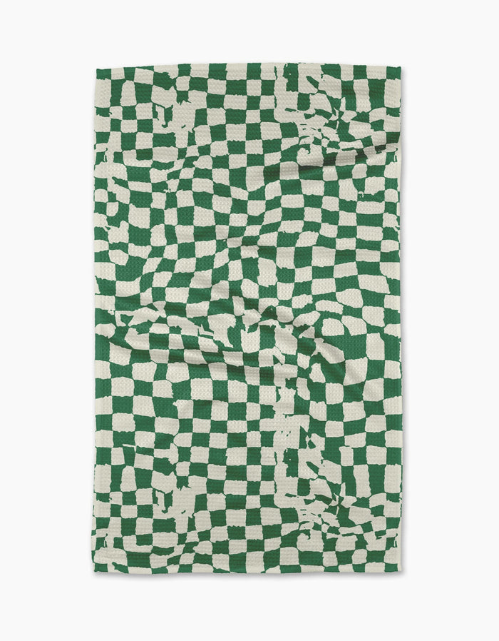 The Geometry Verdant tea towel is a rectangular, eco-friendly towel featuring a green and white distorted checkerboard with irregular lines and random splotches. Made from absorbent fabric, it’s shown slightly creased against a white background.