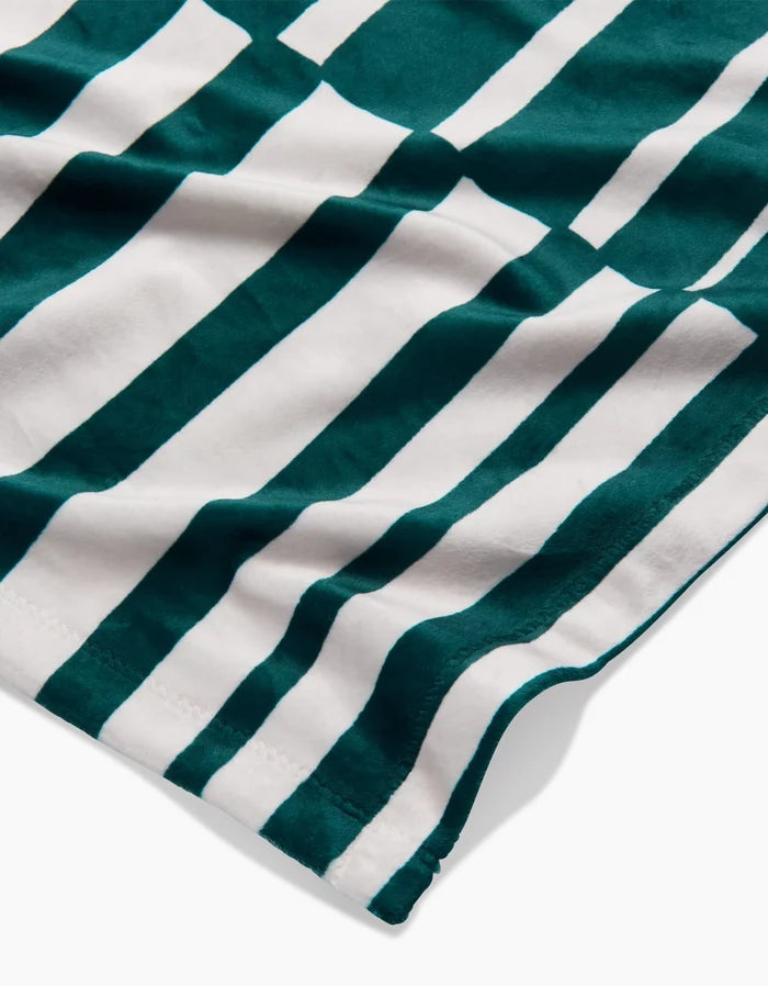 A close-up of Geometrys Verdelia fabric, showcasing alternating dark green and white vertical stripes with a subtly wavy, silky texture and visible edge stitching.