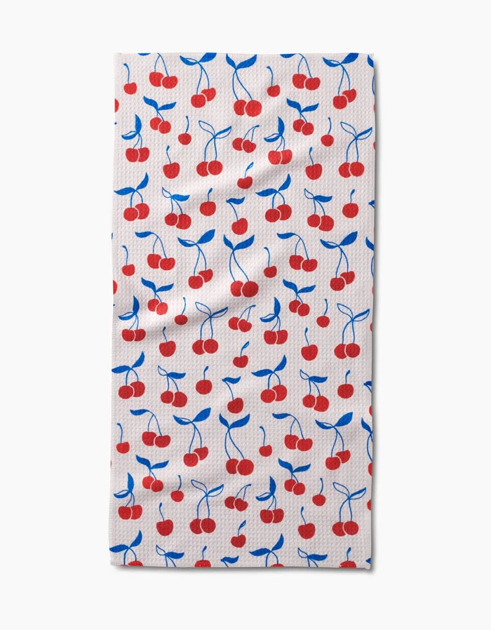 The Kayla Ann Very Cherry Bar Towel is rectangular and white, featuring red cherries with blue stems and leaves on Geoweave fabric for extra absorbency and durability.