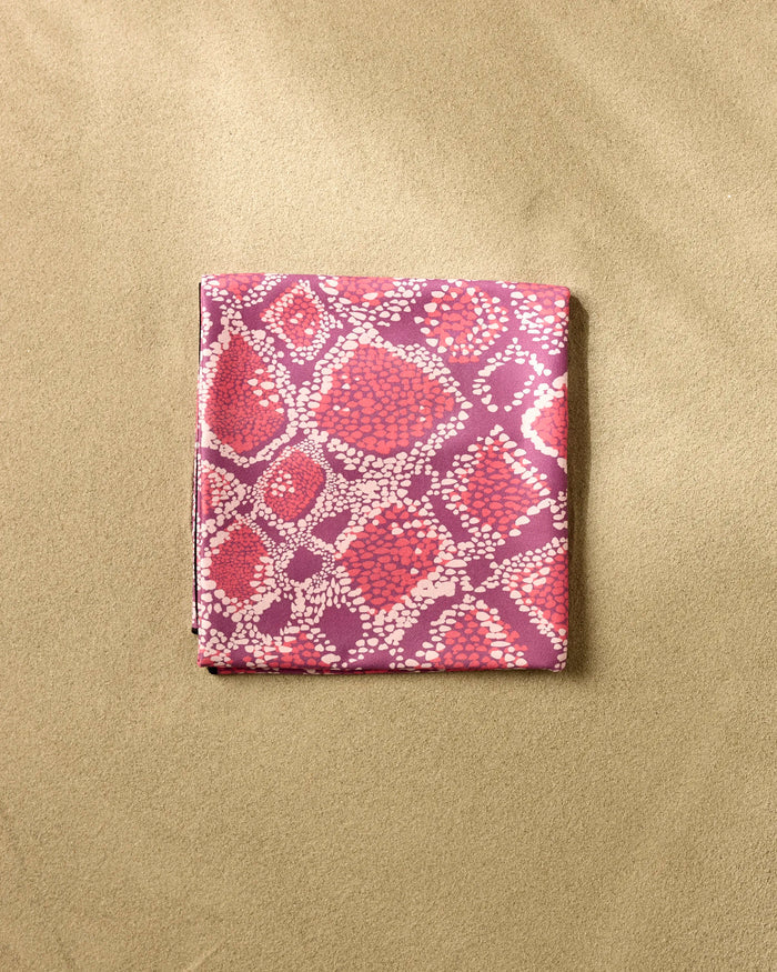 The Elisabeth Wing Vibrant Venom is a folded fabric featuring a pink and purple abstract dotted pattern, set on a textured beige background, perfect as a stylish quick-drying beach blanket.