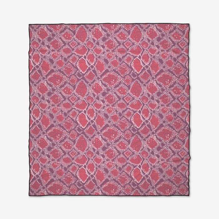 The Elisabeth Wing Vibrant Venom Micro-loop Beach Blanket is square, quick-drying, and made from recycled materials. It features a geometric pattern of red, pink, and purple diamonds and ovals on white with black edges.