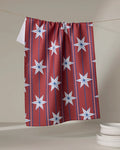 The Ashley Celena Vintage Stars tea towel, featuring blue and white star patterns and vertical stripes, hangs on a clothesline above a stack of white plates. Its quick-drying design adds convenience to your kitchen.