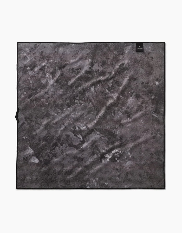 The Geometry Wag Wise towel is a square, highly absorbent towel with a black and gray abstract pattern, featuring a small black label in the upper right corner and a subtle left-edge tag. Shown laid flat on a white background.