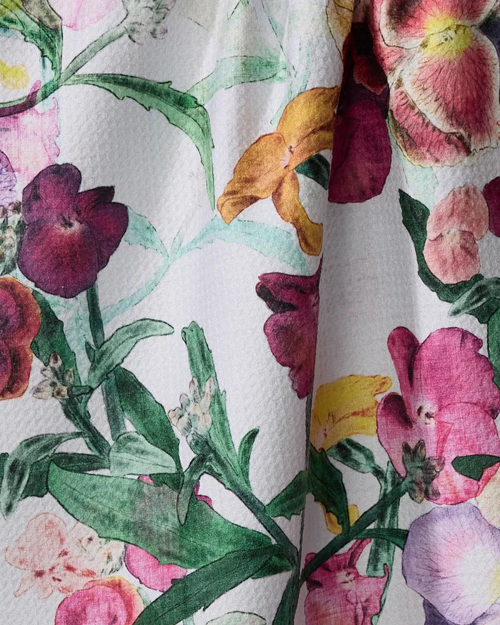 Close-up of Wallflower by Pascale Dilger: an ultra-absorbent tea towel made from recycled materials, featuring textured white fabric with a colorful floral print of green leaves and vibrant red, pink, yellow, and purple flowers.