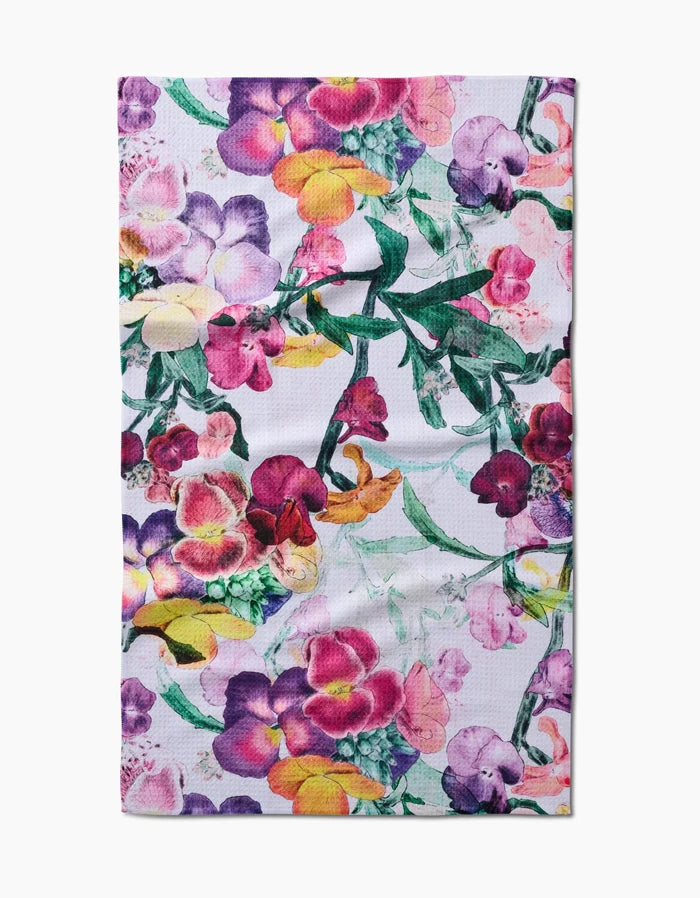 The Wallflower towel by Pascale Dilger features a vibrant floral pattern in purple, pink, yellow, and green on ultra-absorbent Geoweave fabric with a white background.