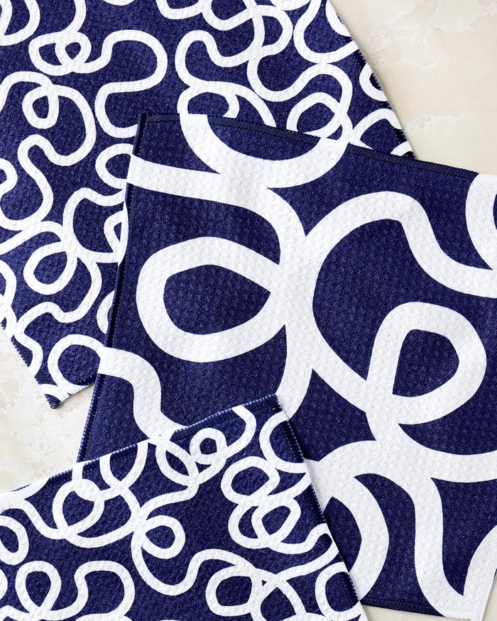 Three "Wander" dishcloths by Rachel Parker in navy blue, each featuring bold white squiggly lines, are shown overlapping on a light surface.