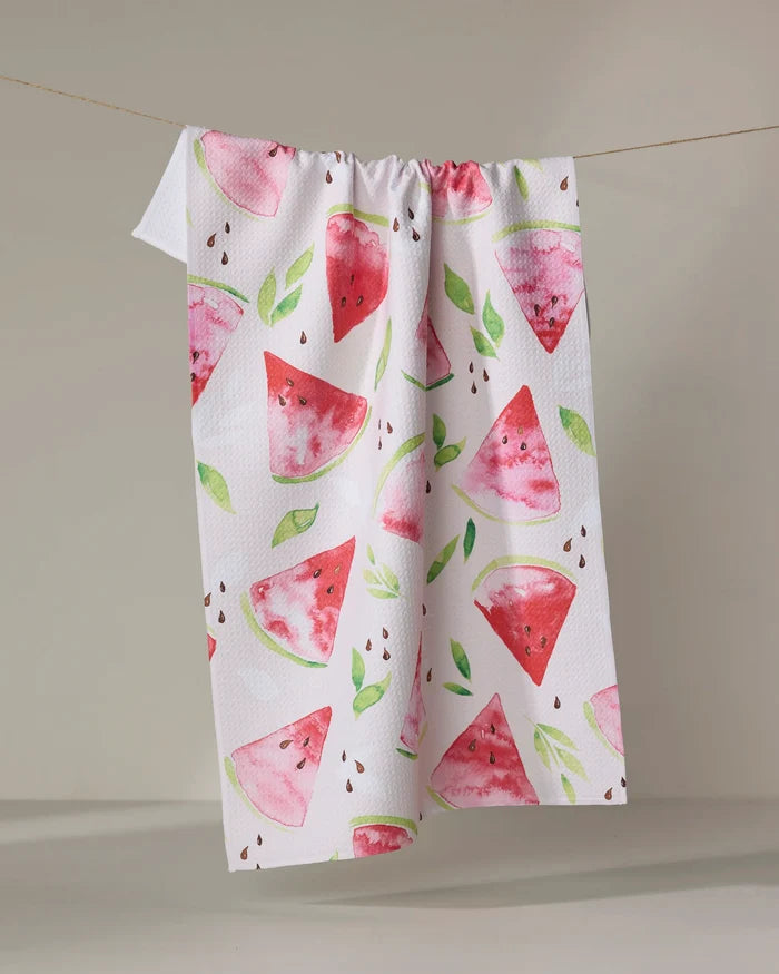 The Watermelon Slice towel by Elena Fay features a white, ultra-absorbent fabric with a vibrant watercolor design of watermelon slices, green leaves, and seeds, shown hanging on a line against a neutral background.