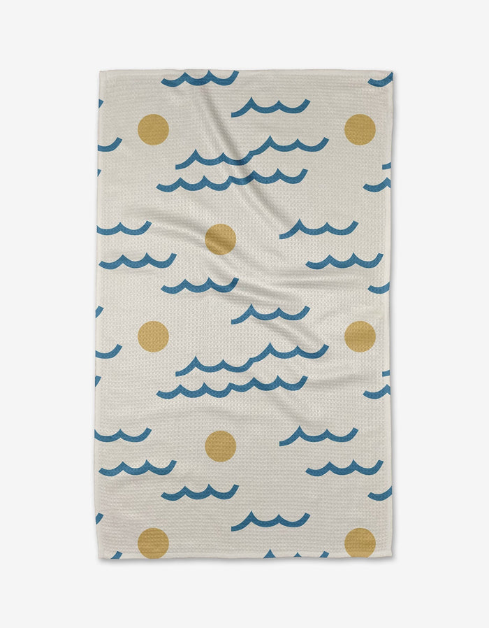 The Wavy Day Tea Towel by Elizabeth Edwards, in beige and made from recycled materials, showcases blue wavy lines and yellow circles reminiscent of waves and suns, displayed flat on a white background.