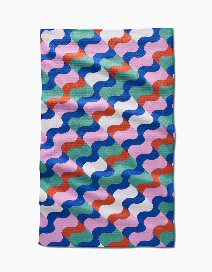 The Claire Iglesias Wavy Stripes Tea Towel features a wavy, interlocking blue, green, pink, red, and white pattern on Geoweave fabric. Its rectangular shape and subtly uneven edges highlight the towels texture and quality.