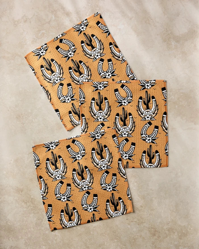 Three pieces of Cole Strem’s Western Horseshoes faux leather, made from recycled materials and featuring a black and white pattern of horseshoes, stars, and western hats, are displayed on a light marble surface.