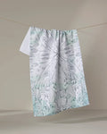 Skye Walker's "Whale" tea towel, crafted from recycled materials, features a light abstract nature design in pale green and gray, displayed on a line against a neutral background.