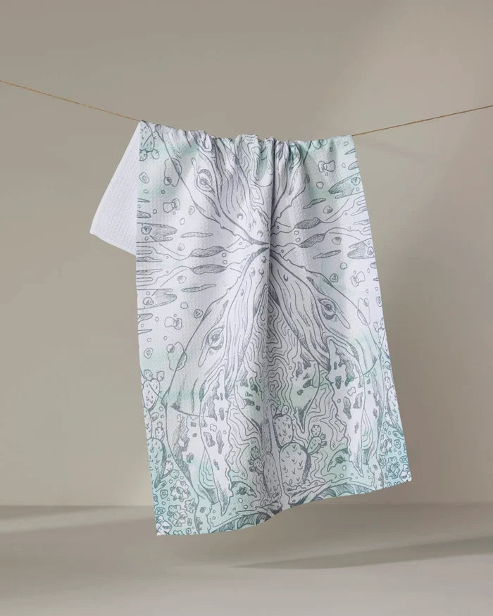 Skye Walker's "Whale" tea towel, crafted from recycled materials, features a light abstract nature design in pale green and gray, displayed on a line against a neutral background.