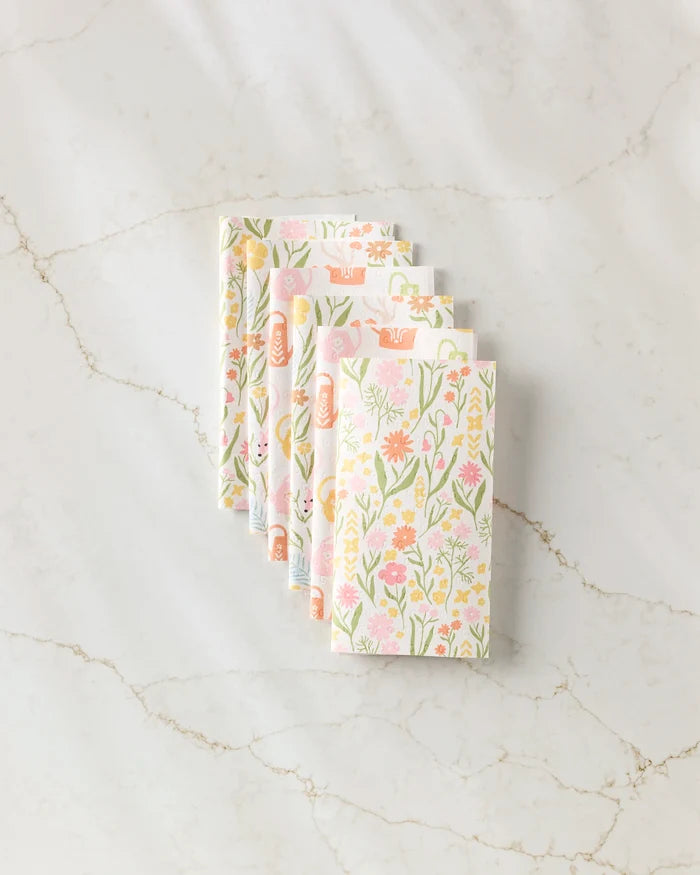 Five "Whimsy and Retro" napkins by Kayla Ann, featuring a pastel floral pattern on eco-friendly paper, are folded in a fan shape and displayed on a white marble surface with subtle gray veining.