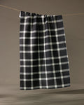The Geometry Wicklow Black kitchen towel, featuring a black and white checkered pattern, hangs on a clothesline against a simple, neutral background.
