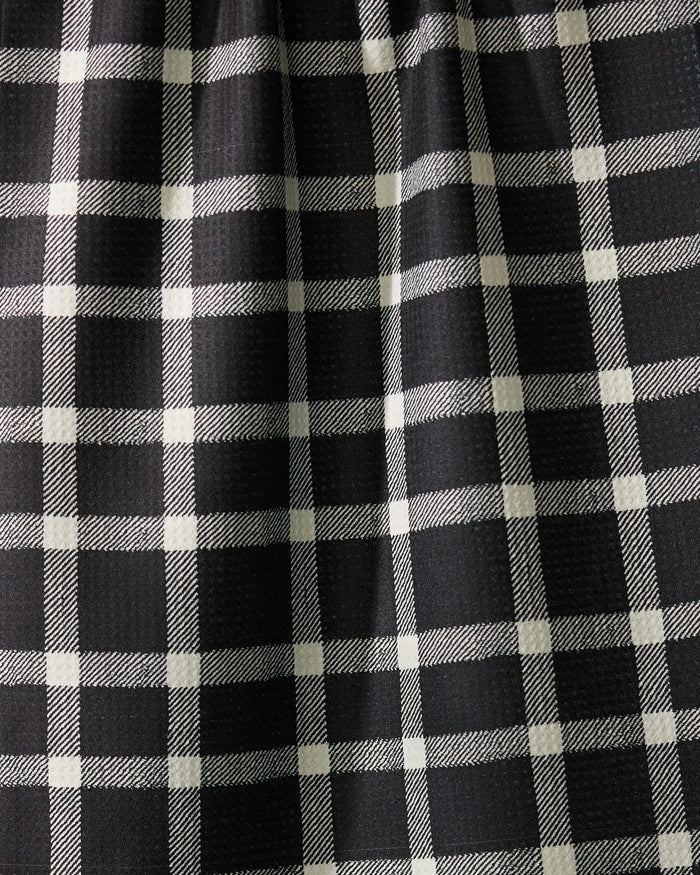 Close-up of Geometrys Wicklow Black: black fabric with a white plaid pattern, slightly gathered to form gentle vertical folds and subtle shadows across the grid design.