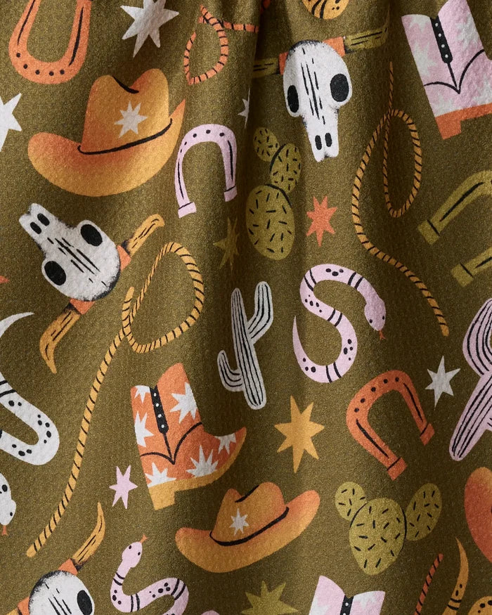 The Wild Cowboy kitchen tea towel by Megan Roy is made from recycled materials and features a Western pattern with cowboy hats, boots, cacti, steer skulls, lassos, and stars in orange, pink, white, and black on olive green.