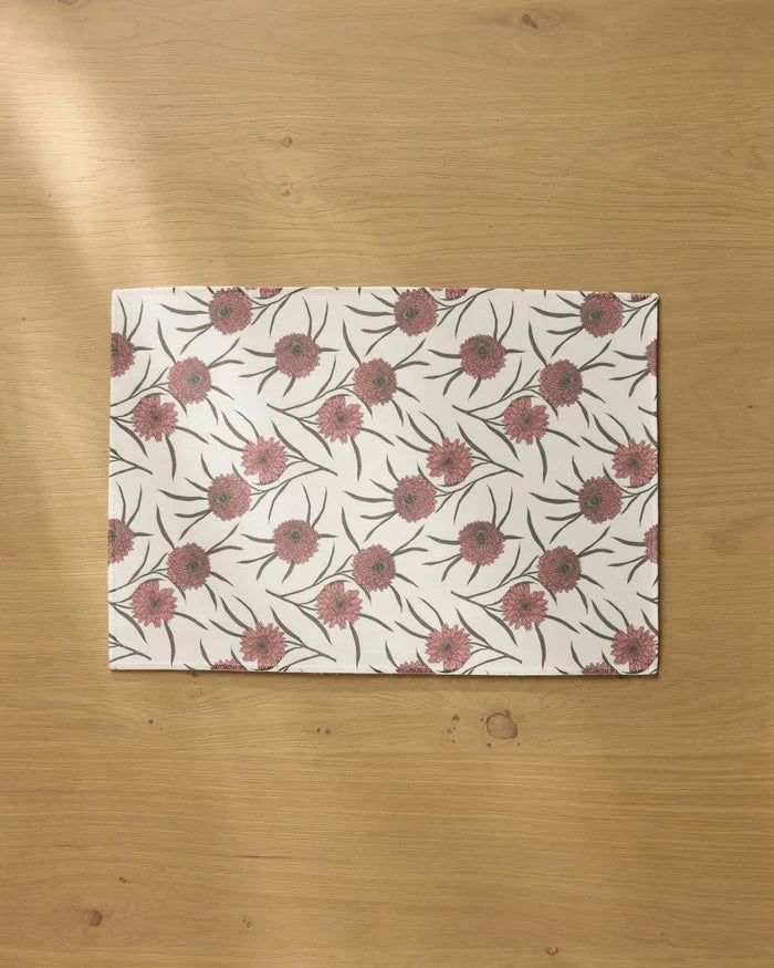 The Wild Dahlia placemat by Geometry features a pink and green floral pattern on a white background, displayed on a light wooden table.