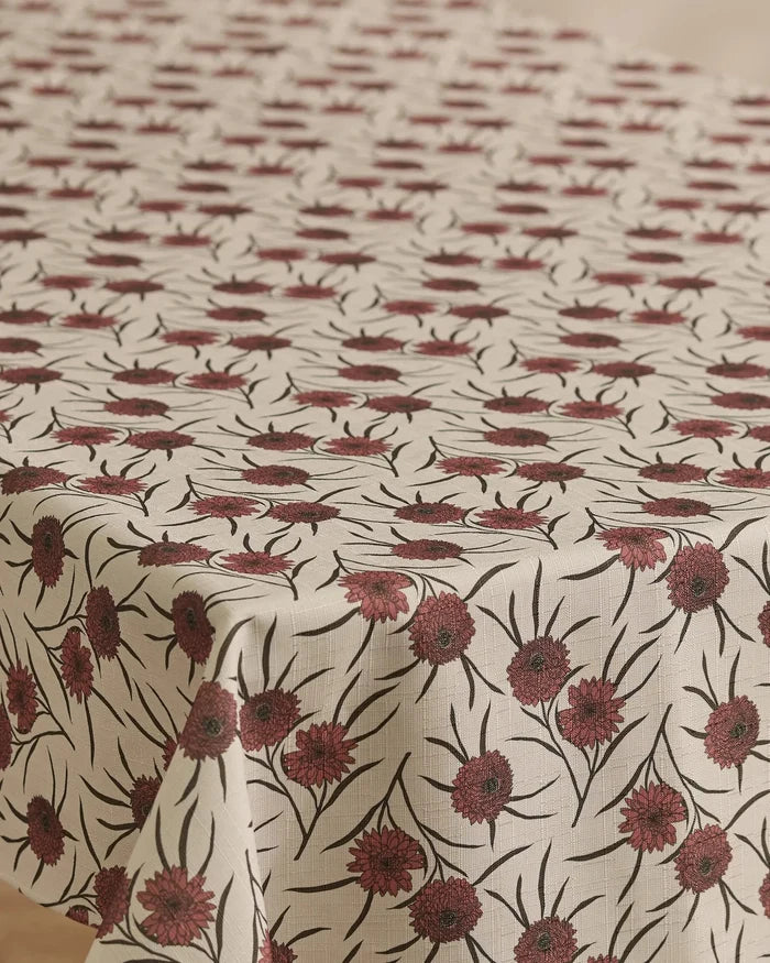 A rectangular table with Geometry’s Wild Dahlia stain-resistant cream tablecloth, featuring a repeating pattern of red flowers with dark centers and green stems and leaves.