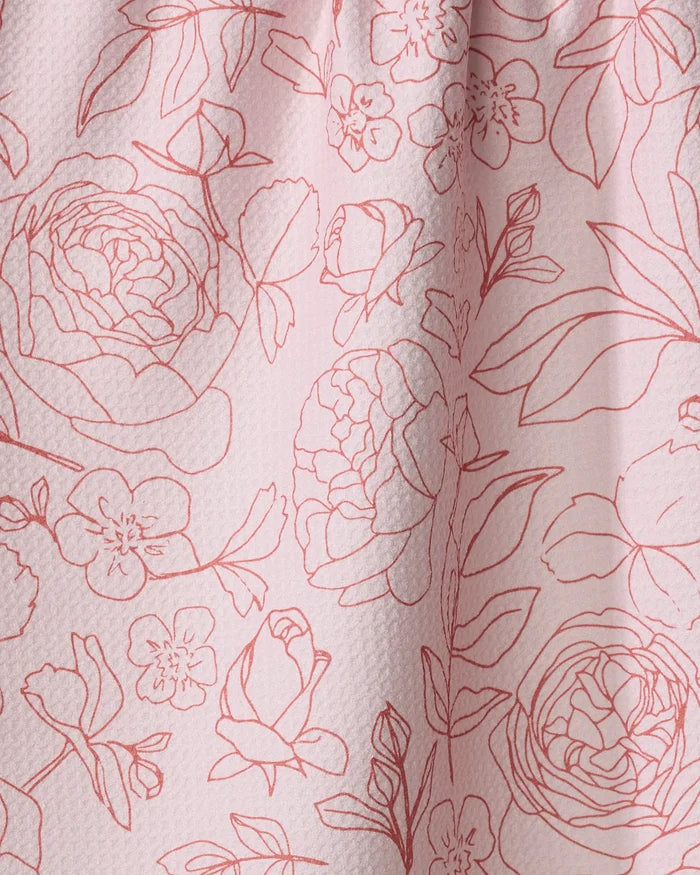 The "Wild Roses" dish towel by Janna Sue Design features pink textured fabric with a red floral outline of roses, peonies, leaves, and buds. Absorbent cotton and subtle folds highlight the elegant surface pattern.