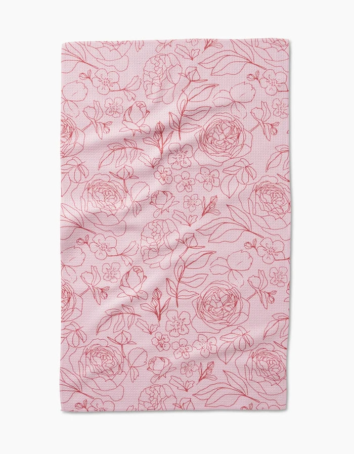The Wild Roses tea towel by Janna Sue Design is pink and rectangular, adorned with red-outlined flowers and leaves across its recycled material surface.