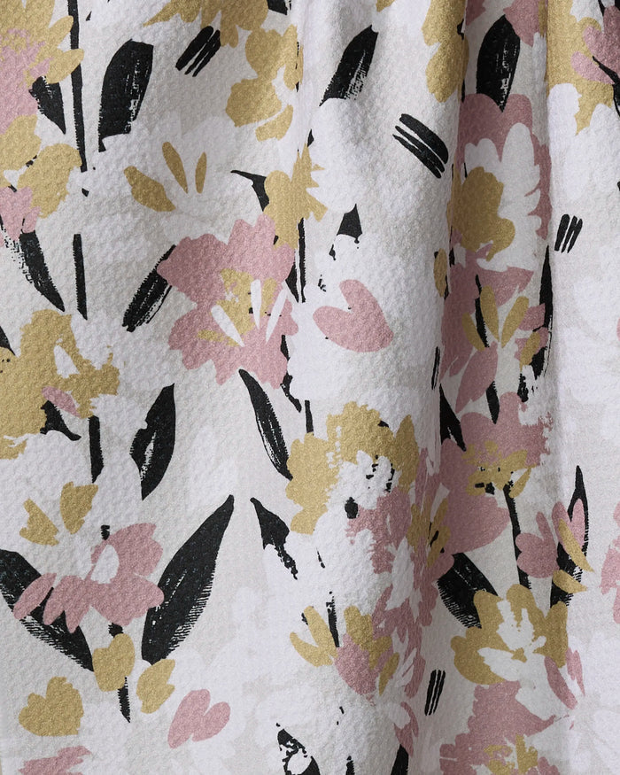 Close-up of the Toboggan Avenue "Wilderness Floral" quick-drying towel with yellow, pink, and black abstract flowers and leaves on a textured white background.