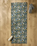 The Danelys Sidron Wildflower Vine Blush yoga mat, featuring white, blue, and yellow flowers, rests on a light wooden floor with a non slip towel, a white water bottle at one end, and two gray yoga blocks nearby.