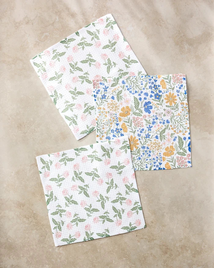 Three Danelys Sidron "Wildflower Vine Blush" paper napkins rest on a beige surface: two with green and pink leaves, one with yellow, blue, and green florals—crafted from recycled materials for an eco-friendly touch.