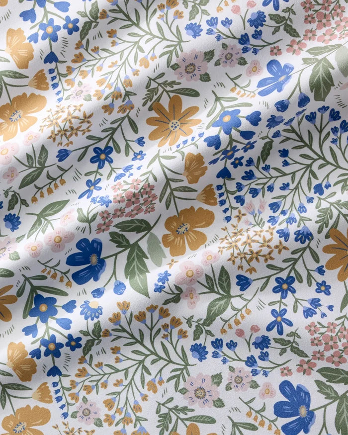 A close-up of Danelys Sidron’s Wildflower Vine Blush shows a colorful floral pattern on Geosuede fabric. Blue, yellow, pink, and green flowers on white with gentle wrinkles—perfect for vibrant dinner napkins.