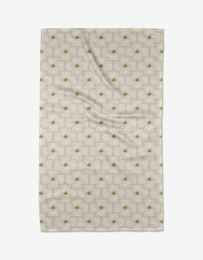 The Ash Cascade Wildflower tea towel is a beige rectangle made from Geoweave fabric, decorated with a white geometric pattern and small green floral accents, shown flat on a white background.