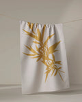The PrintedPlant Willow towel, featuring a large golden bamboo leaf design, dries quickly and hangs on a clothesline against a neutral background.