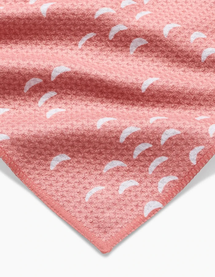 A close-up of the Windswept towel by Jessica Swift: a textured pink waffle weave made from recycled materials, featuring white crescent shapes and a neatly finished edge visible in the lower corner.
