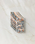 A stack of GEOMETRY’s Wings in the Wind patterned napkins, featuring an abstract butterfly wing design in orange, black, and white, crafted from eco-friendly kitchen towels and displayed on a light marble surface.