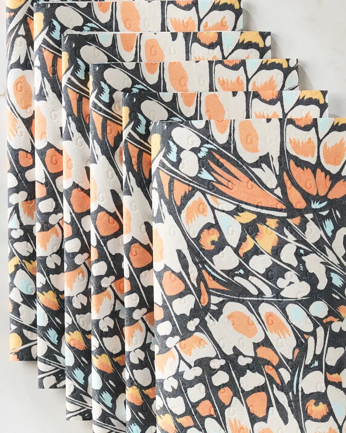 GEOMETRY’s “Wings in the Wind” recycled paper towels are fanned out on a neutral background, each showcasing a vibrant butterfly wing pattern in orange, black, cream, and light blue.