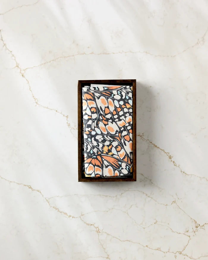The GEOMETRY "Wings in the Wind" rectangular bar soap, featuring a detailed black, white, and orange butterfly wing design, sits on light marble near eco-friendly kitchen towels for a sustainable accent.