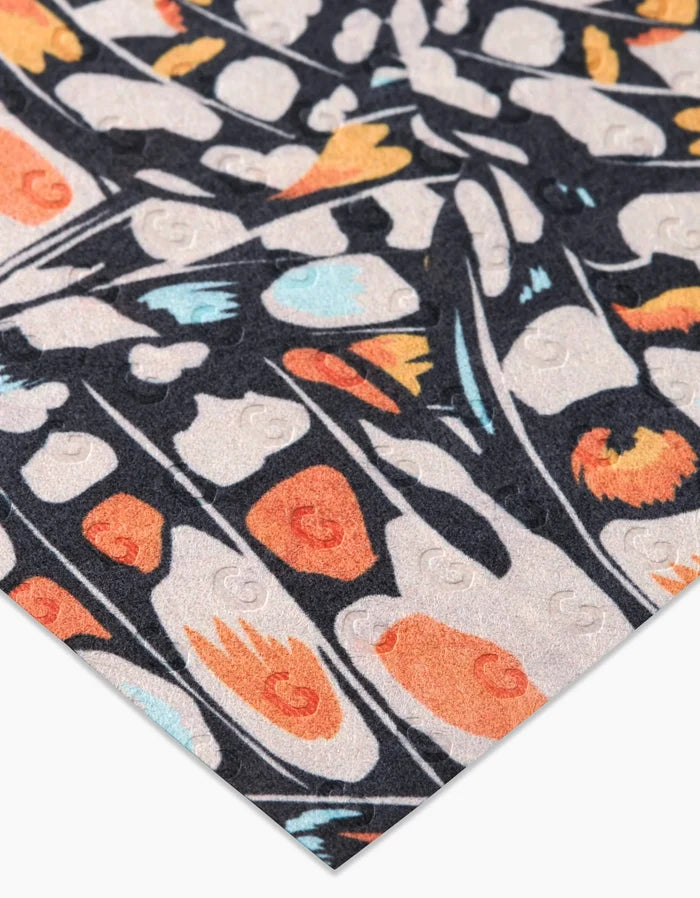 A close-up of GEOMETRY’s Wings in the Wind paper, featuring abstract orange, black, white, and blue designs with subtle embossed circles. Made from post-consumer recycled materials in a repeating geometric pattern.