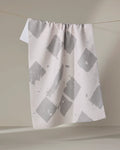 The Geometry Wisp Gray recycled kitchen towel, featuring large irregular gray squares on white, hangs on a clothesline against a neutral background.