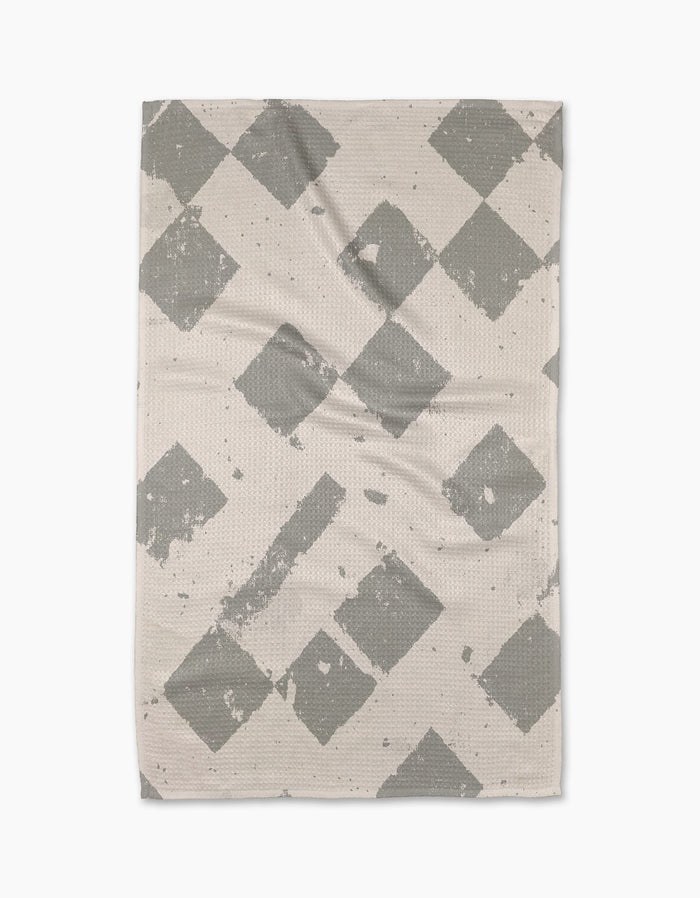 The Geometry Wisp Gray tea towel is rectangular and beige, featuring a gray diamond pattern with faded, distressed details, displayed flat on a white background.
