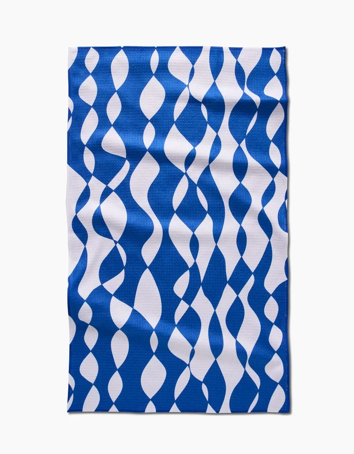 The Claire Iglesias Wonky Lines tea towel features a blue and white wavy ribbon pattern on durable Geoweave fabric, shown laid flat on a white background.