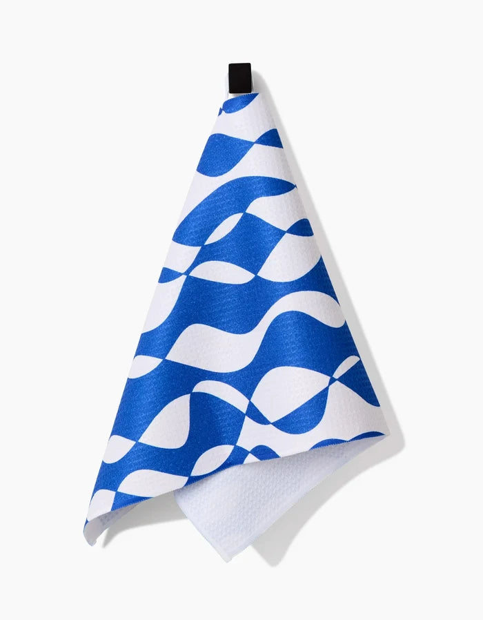 The Claire Iglesias Wonky Lines bar towel, crafted from Geoweave fabric, displays a wavy abstract blue and white pattern and hangs on a black loop against a white background.