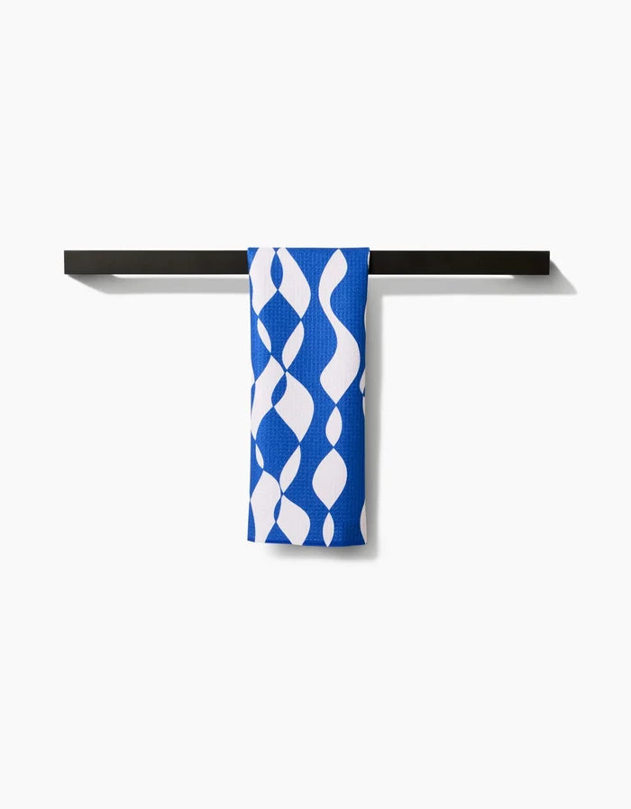The Wonky Lines bar towel by Claire Iglesias features a blue and white wavy abstract pattern. Made from premium Geoweave fabric, its draped over a black towel bar and combines modern style with superior absorbency.