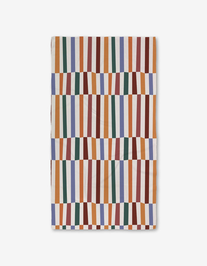 The Claire Iglesias Wonky Stripes textile showcases vertical orange, green, blue, red, and mustard stripes with a wavy geometric pattern on white, crafted with ultra-absorbent Geoweave technology for superior performance.