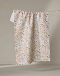 The Woodland Floral tea towel by Hufton Studio, featuring a soft beige, orange, and blue floral pattern, hangs on a clothesline against a neutral background.
