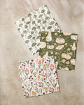 The Kayla Ann Woodland Trail set features three recycled patterned cloths: green mushrooms, orange pumpkins with vines on green, and small colorful flowers and leaves, displayed on a beige surface.