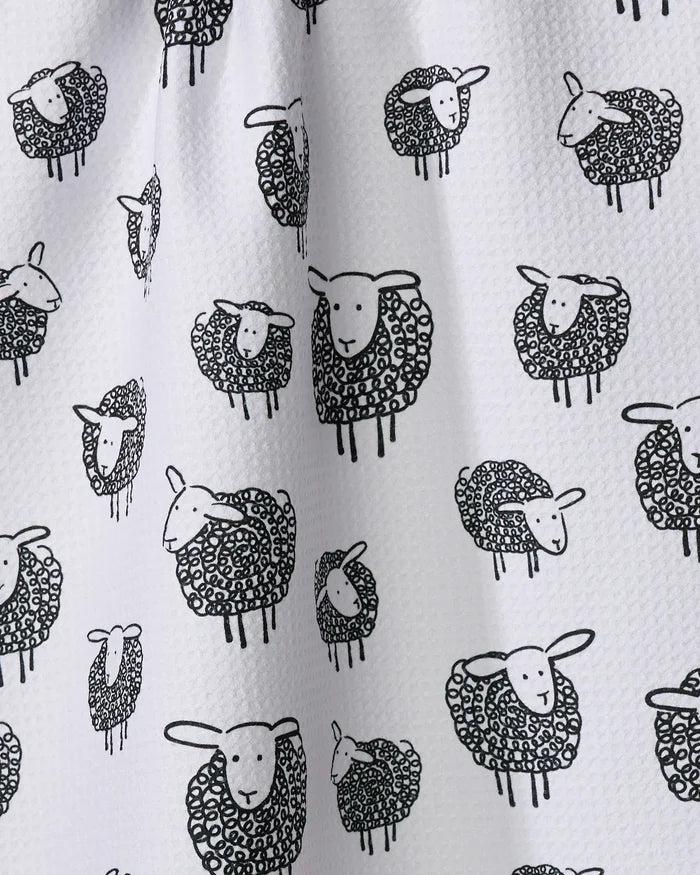 The Kris Ruff Wooly Sheep tea towel features a white textured fabric with a repeating pattern of black-outlined cartoon sheep, each with a curly, shaded body and simple facial features.