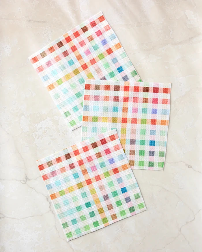 The Pascale Dilger Woven Spring Plaid set includes three square, super-absorbent dishcloths with a colorful plaid pattern, displayed on a light marble surface.
