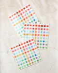 The Pascale Dilger Woven Spring Plaid set includes three square, super-absorbent dishcloths with a colorful plaid pattern, displayed on a light marble surface.