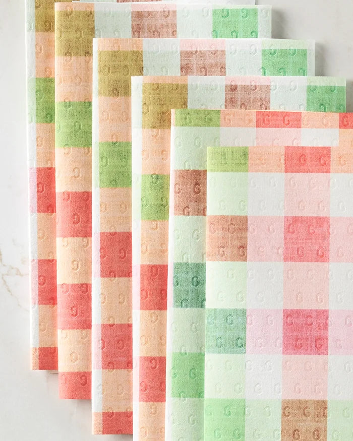 Five Pascale Dilger Woven Spring Plaid eco-friendly paper towels, featuring a pastel checkered pattern in pink, green, orange, and beige with a subtle embossed G design, are arranged fan-shaped on a white surface.