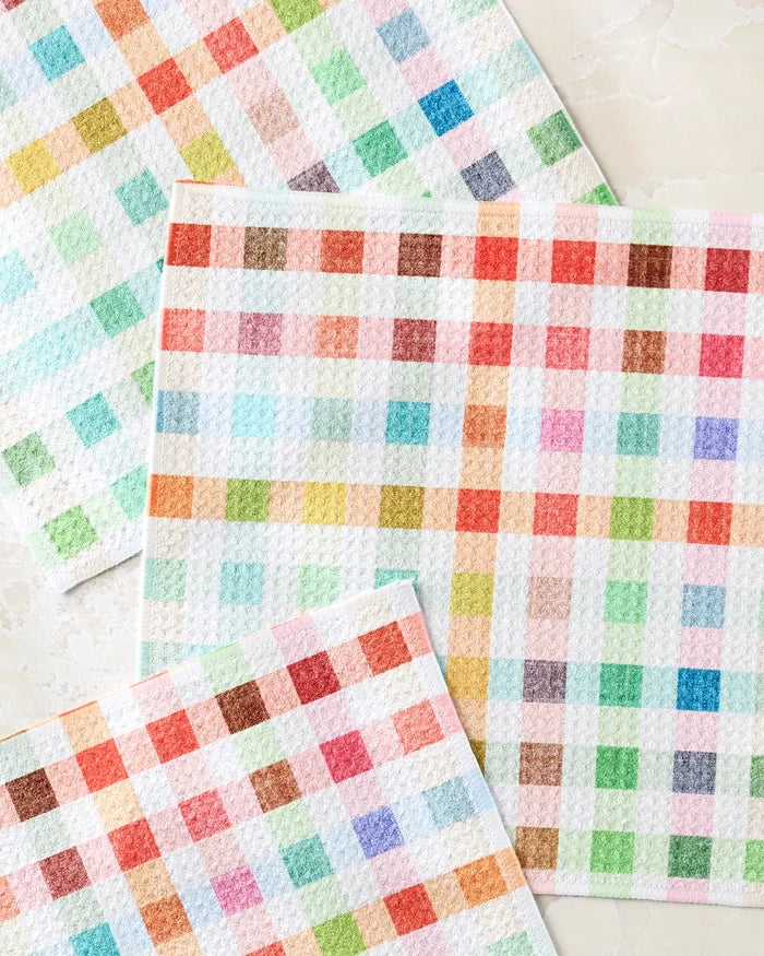 Three textured Woven Spring Plaid dishcloths by Pascale Dilger, each super-absorbent with a checkered pattern in red, blue, green, and orange, are displayed overlapping on a light surface.