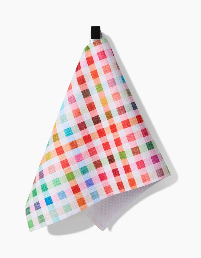 The Pascale Dilger Woven Spring Plaid bar towel, made from recycled materials, features a vibrant red, pink, orange, blue, green, and white checkered pattern and hangs from a black loop against a white background.