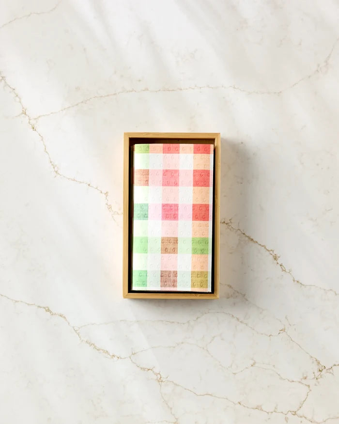A rectangular box of Pascale Dilger’s Woven Spring Plaid eco-friendly paper towels, neatly stacked in pastel plaid, sits on a marbled white surface with subtle gold veining.